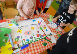 Dzieci dekorują plakat, naklejają kolorowe elementy z papieru.
